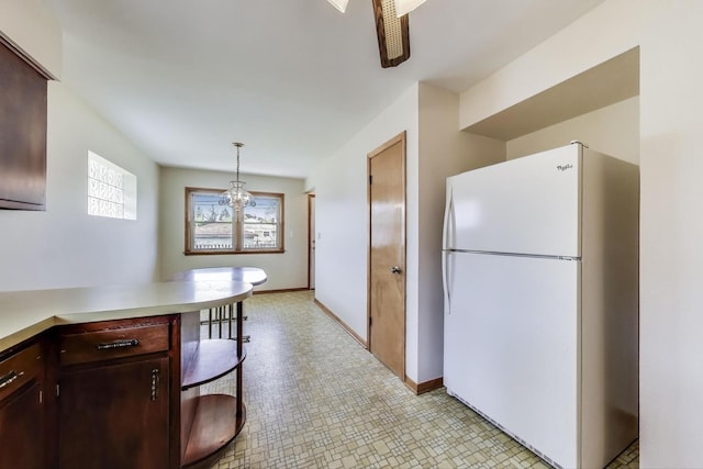 kitchen with freestanding refrigerator, light countertops, a chandelier, light floors, and hanging light fixtures