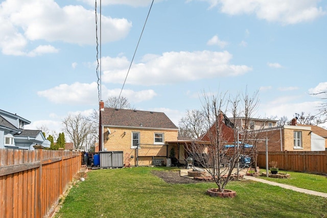back of property featuring a fenced backyard, a yard, and brick siding