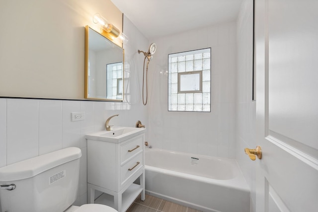 bathroom featuring toilet, tile walls, shower / washtub combination, and vanity