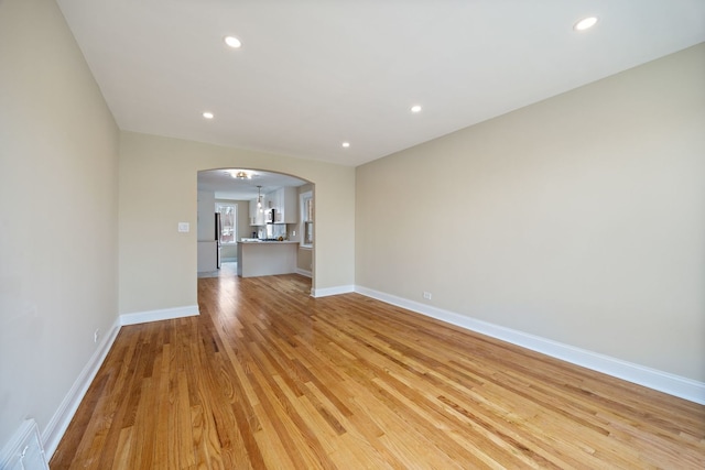 unfurnished living room with arched walkways, baseboards, recessed lighting, and light wood finished floors