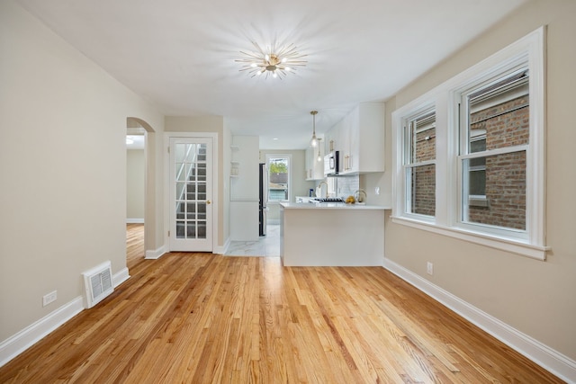 unfurnished living room with visible vents, arched walkways, light wood finished floors, and baseboards
