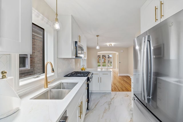 kitchen featuring appliances with stainless steel finishes, hanging light fixtures, arched walkways, a sink, and white cabinetry