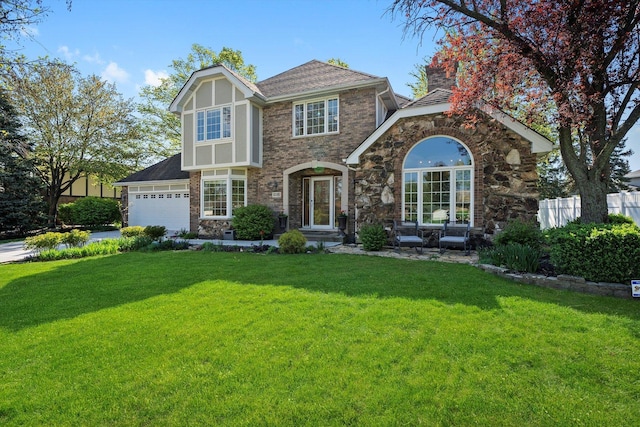 tudor-style house with a front yard, brick siding, driveway, and a shingled roof
