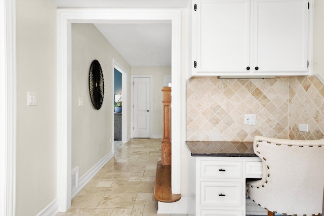 kitchen with baseboards, backsplash, white cabinetry, light stone finish floors, and dark countertops