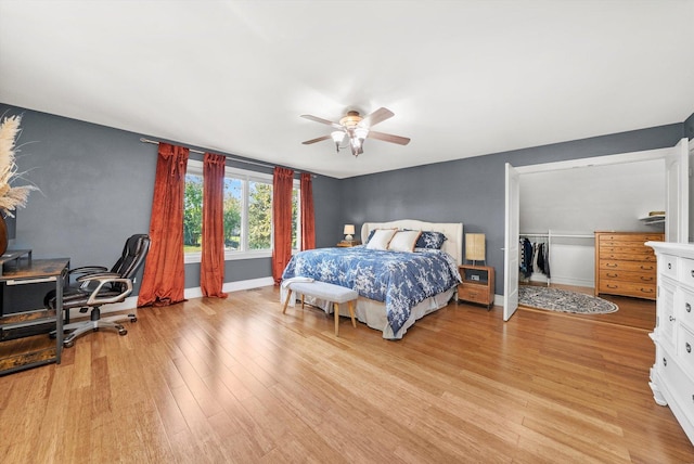 bedroom featuring light wood finished floors, baseboards, an office area, a ceiling fan, and a closet