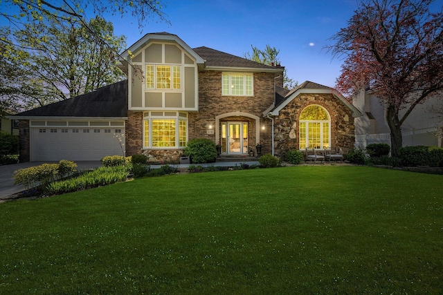 tudor-style house with a lawn, an attached garage, driveway, stone siding, and brick siding