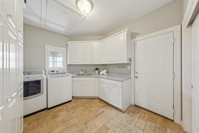 clothes washing area featuring attic access, cabinet space, a sink, light wood-style flooring, and washer and dryer