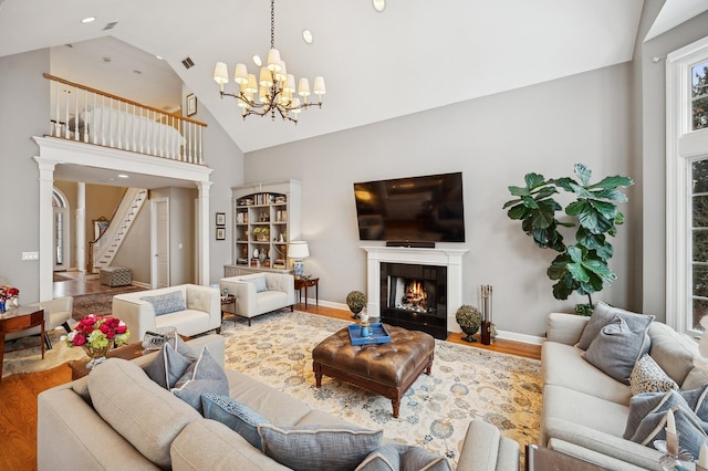living room with wood finished floors, baseboards, high vaulted ceiling, a tile fireplace, and a notable chandelier