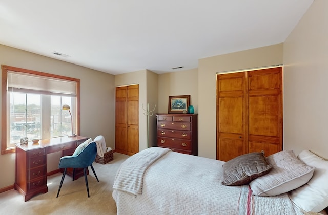 bedroom featuring visible vents, multiple closets, baseboards, and light carpet