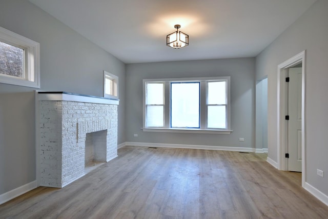 unfurnished living room featuring baseboards, a brick fireplace, and wood finished floors