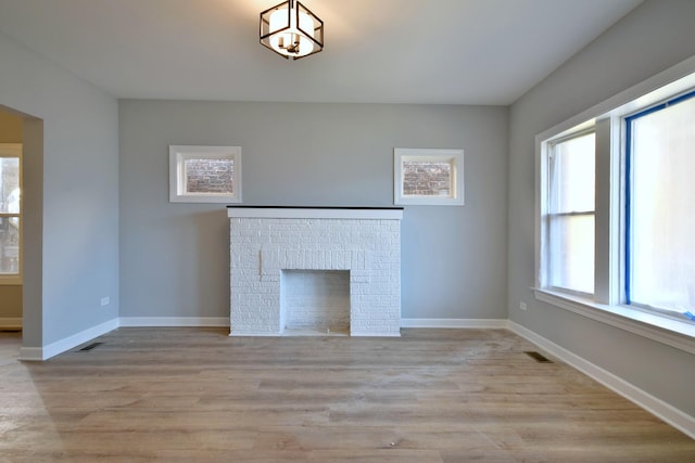unfurnished living room with a brick fireplace, baseboards, visible vents, and light wood-style floors