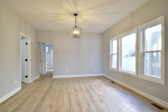 spare room featuring baseboards, a notable chandelier, light wood-style flooring, and visible vents