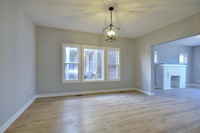 unfurnished dining area with baseboards, a brick fireplace, wood finished floors, and a chandelier
