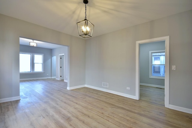 empty room with baseboards, wood finished floors, and a chandelier