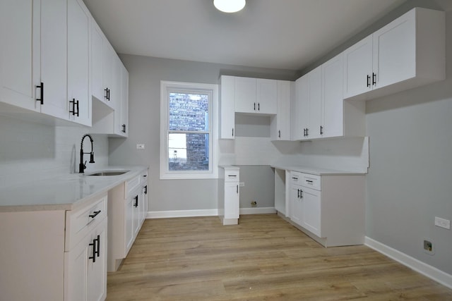 kitchen with light wood-style floors, a sink, baseboards, and decorative backsplash