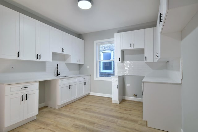 kitchen featuring baseboards, light wood finished floors, backsplash, and white cabinetry