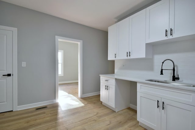 kitchen featuring white cabinetry, a sink, light wood-style flooring, and tasteful backsplash
