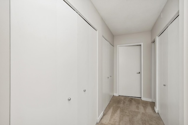 hallway with baseboards and light colored carpet