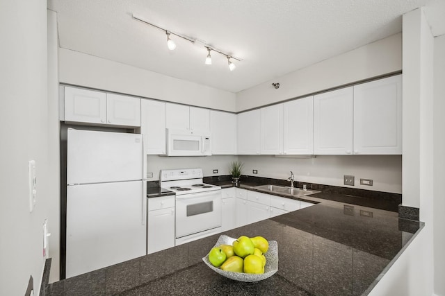 kitchen featuring a peninsula, white appliances, dark stone counters, white cabinetry, and a sink