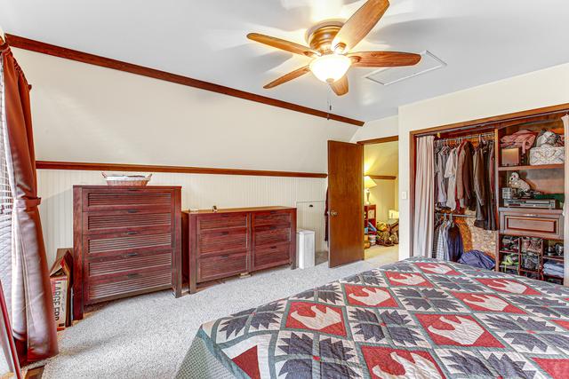 bedroom featuring carpet floors, a closet, attic access, ceiling fan, and a wainscoted wall