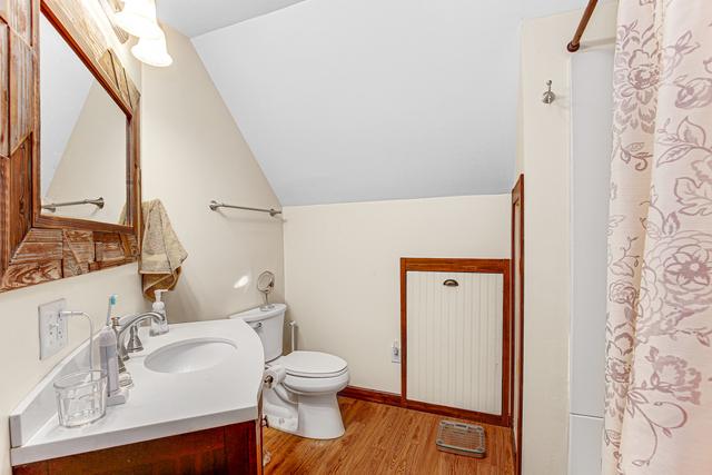 full bath featuring a shower with curtain, wood finished floors, vanity, toilet, and lofted ceiling