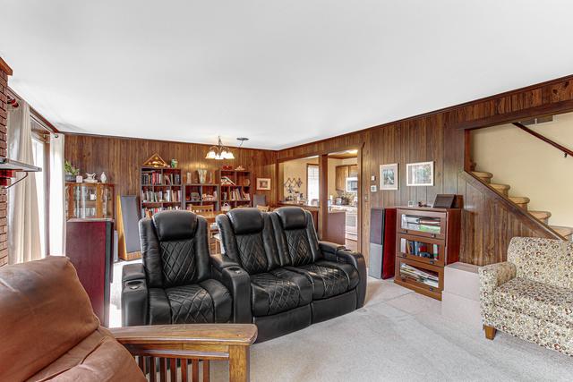 carpeted living area featuring a chandelier, wooden walls, and stairway