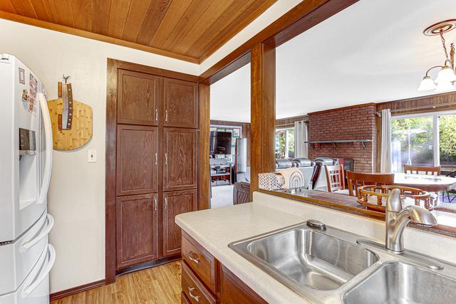 kitchen featuring a sink, white refrigerator with ice dispenser, light countertops, light wood-style flooring, and wooden ceiling