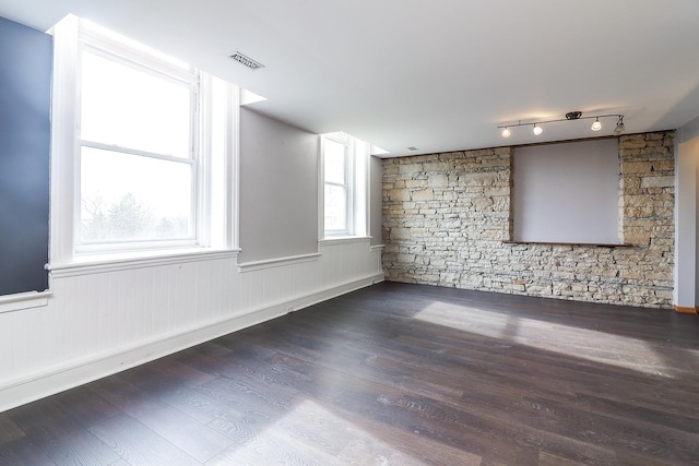 empty room featuring rail lighting, visible vents, wood finished floors, and a wainscoted wall