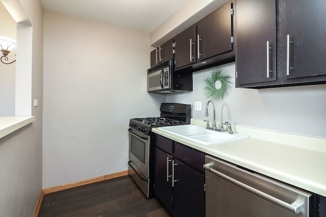 kitchen featuring baseboards, dark wood-style floors, light countertops, a sink, and appliances with stainless steel finishes