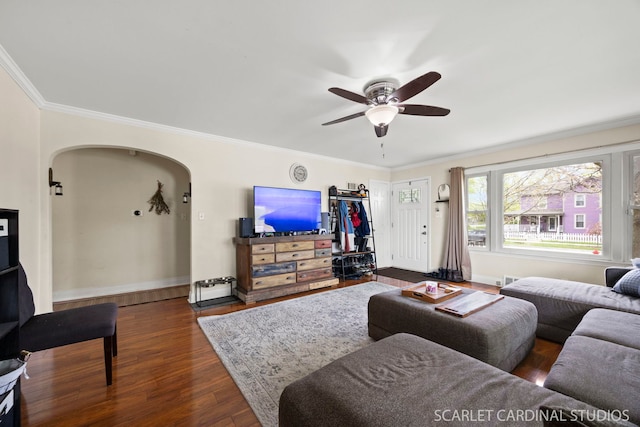 living area with a ceiling fan, dark wood-style flooring, arched walkways, baseboards, and ornamental molding