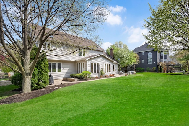 rear view of property featuring a chimney, a lawn, and a patio
