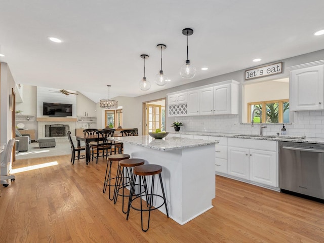 kitchen featuring dishwasher, a fireplace with raised hearth, white cabinetry, a kitchen breakfast bar, and decorative backsplash