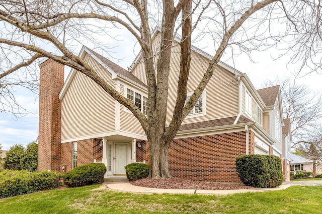 view of home's exterior featuring brick siding, a lawn, roof with shingles, and a chimney