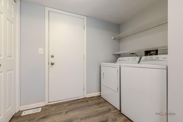 washroom with washing machine and clothes dryer, laundry area, baseboards, wood finished floors, and visible vents