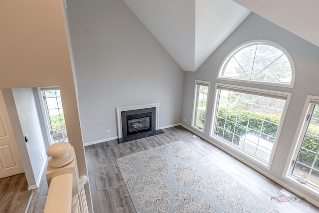 unfurnished living room featuring a fireplace, wood finished floors, a wealth of natural light, and high vaulted ceiling