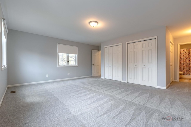 unfurnished bedroom featuring baseboards, carpet floors, two closets, and visible vents