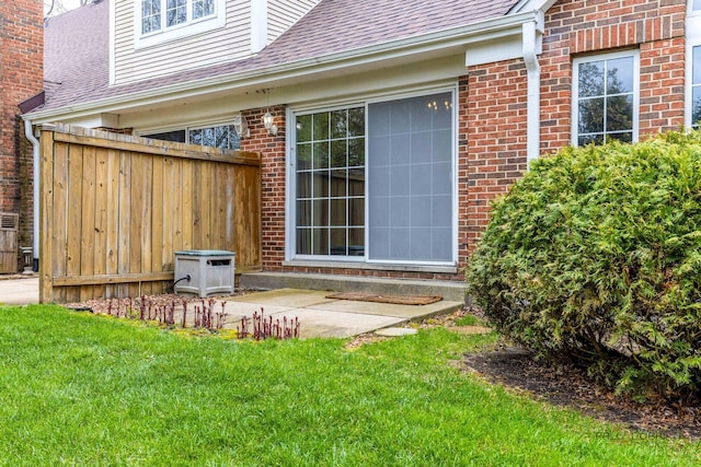 back of house with roof with shingles, a lawn, brick siding, fence, and a patio
