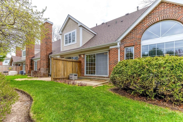 back of property featuring fence, a lawn, central AC, and brick siding