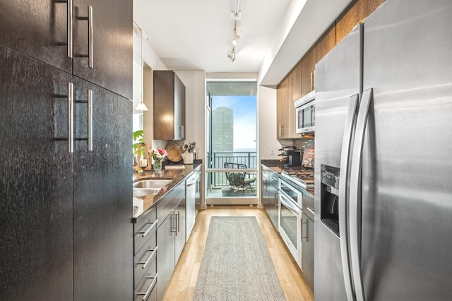 kitchen featuring light wood-style floors, appliances with stainless steel finishes, dark stone countertops, and rail lighting