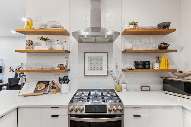 kitchen with wall chimney range hood, open shelves, stainless steel appliances, white cabinetry, and backsplash