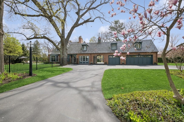 cape cod-style house with brick siding, a front yard, a chimney, and concrete driveway