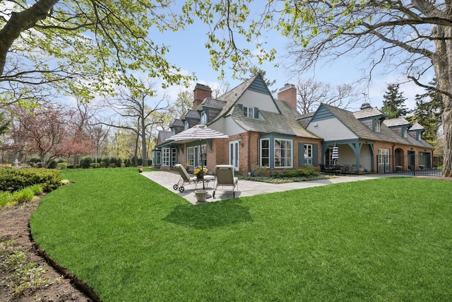 rear view of house with a chimney, brick siding, fence, a yard, and a patio