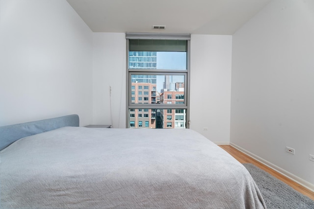 bedroom featuring wood finished floors, expansive windows, and baseboards