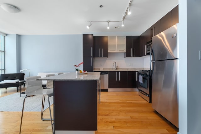 kitchen featuring appliances with stainless steel finishes, a center island, a sink, a kitchen bar, and light wood-style floors