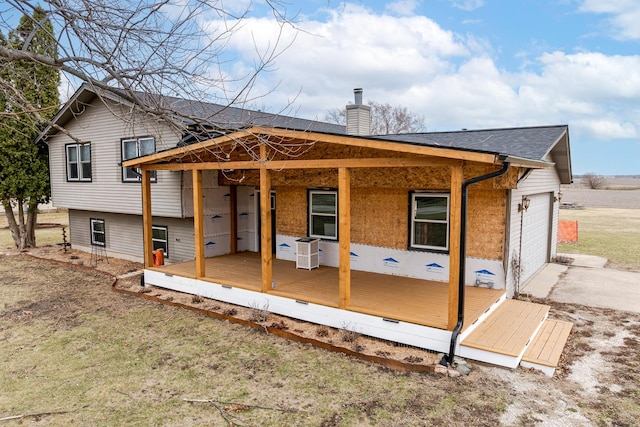 rear view of property featuring a garage, driveway, covered porch, and a chimney