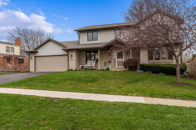 traditional home featuring a porch, a front yard, a garage, brick siding, and aphalt driveway