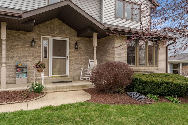 doorway to property with a porch and brick siding