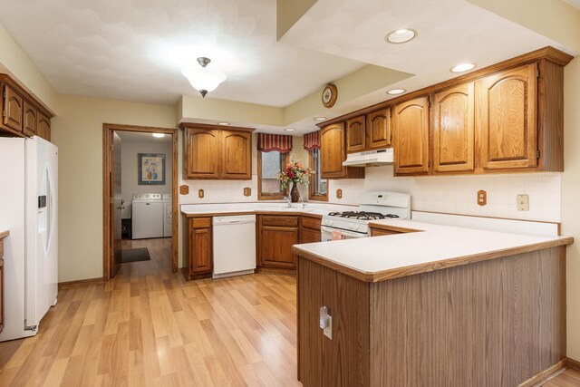 kitchen featuring white appliances, brown cabinetry, washer / clothes dryer, a peninsula, and under cabinet range hood
