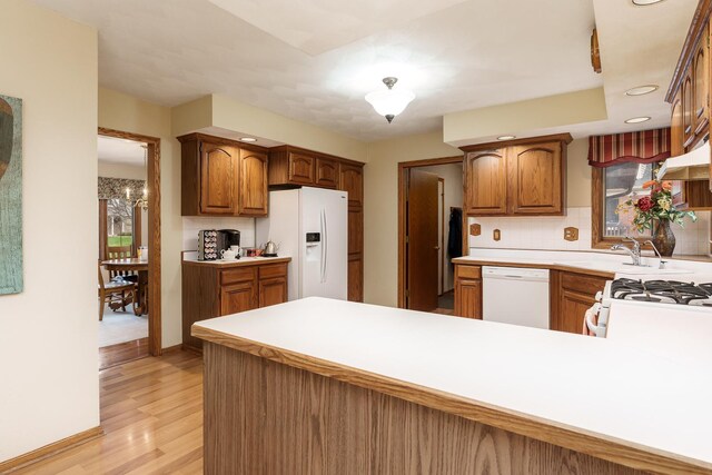kitchen with decorative backsplash, a peninsula, white appliances, light wood-type flooring, and light countertops