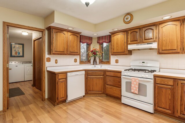 kitchen featuring brown cabinetry, under cabinet range hood, white appliances, and washing machine and clothes dryer